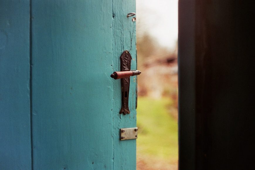 A light blue door cracked open to show the natural world outside.
