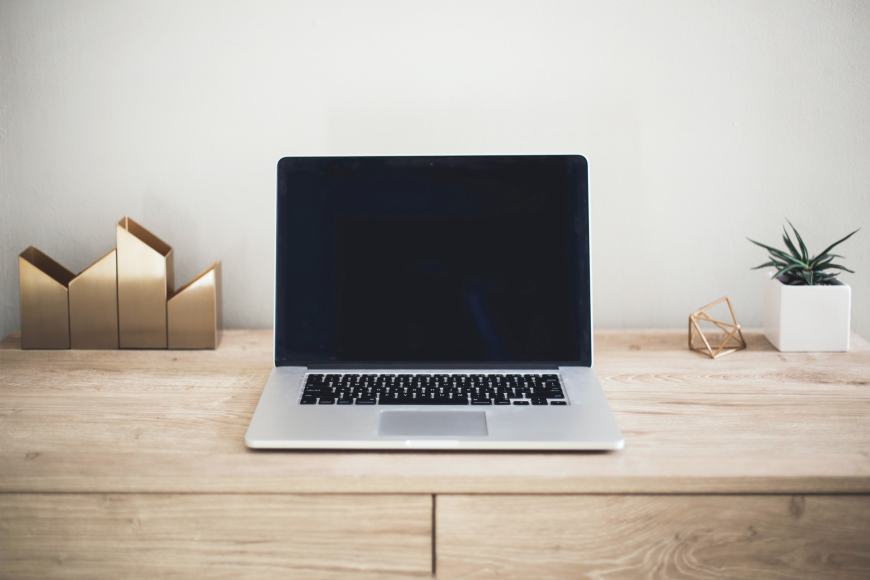 A silver laptop opened up, sitting on a wooden desk, with gold decorations and a small plant in the background.